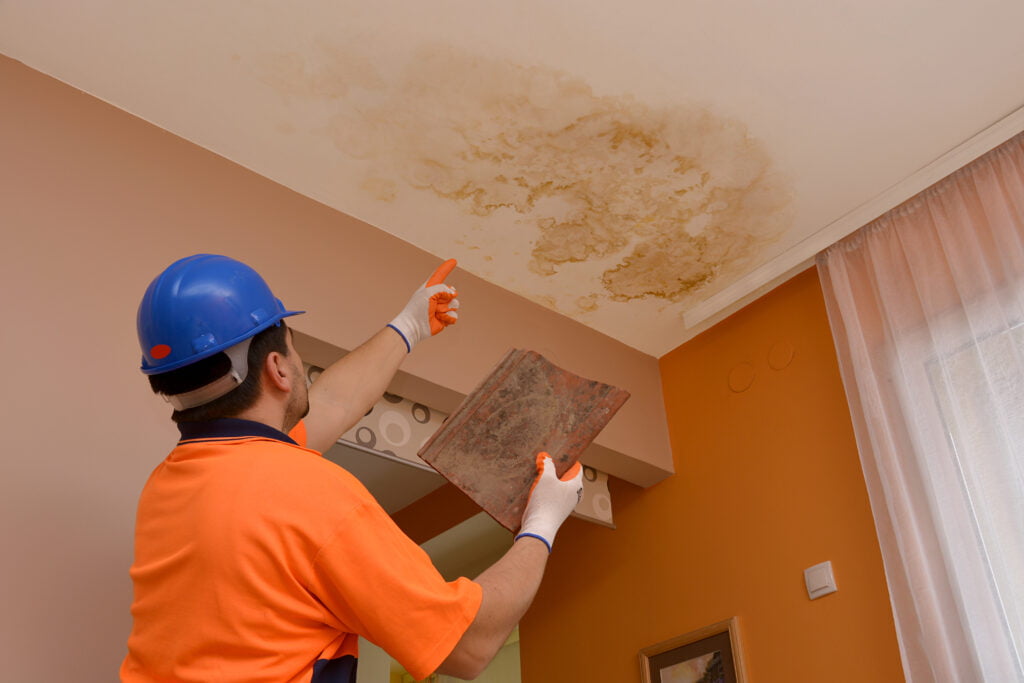 construction worker pointing to water leak mold stain on ceiling from roof leak